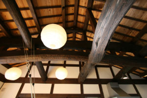 居間の小屋裏：開放感がある居間の小屋裏。梁方向４間、桁方向２間共に一本の松。「太鼓梁」の造作が施してあります。100年以上も前の古材を使用。
