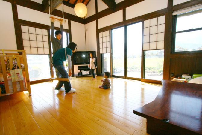 居間：床暖房仕様の居間はよく乾燥させ、狂いの少なくなった桧の無垢板。大きく横たわる梁からは自家製のブランコに子供さんはいつも元気に遊びます。障子は「猫目障子」（全16帖）で開放感抜群です。